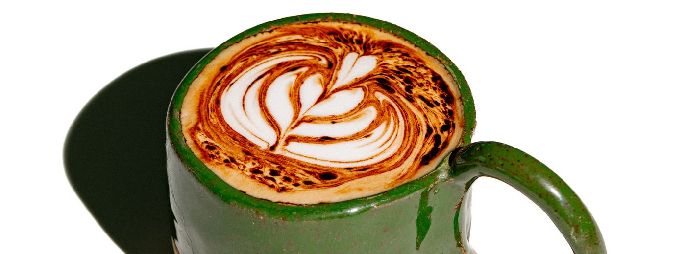 Café com desenho de folha na xícara verde da kolosso